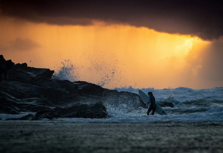 A surfer coming in from the water at dusk