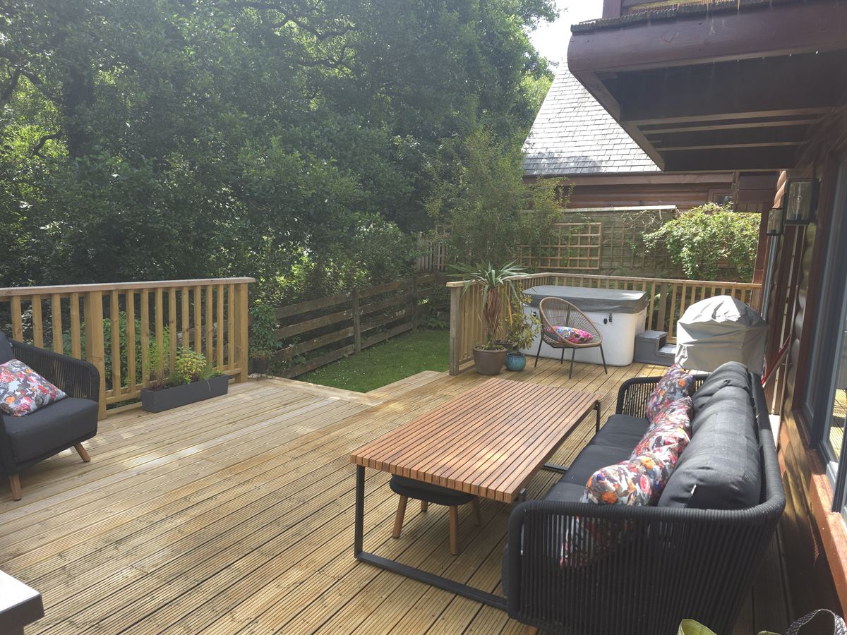 The deck at Creekside Retreat, with seating, a dining table, the hot tub and the garden below